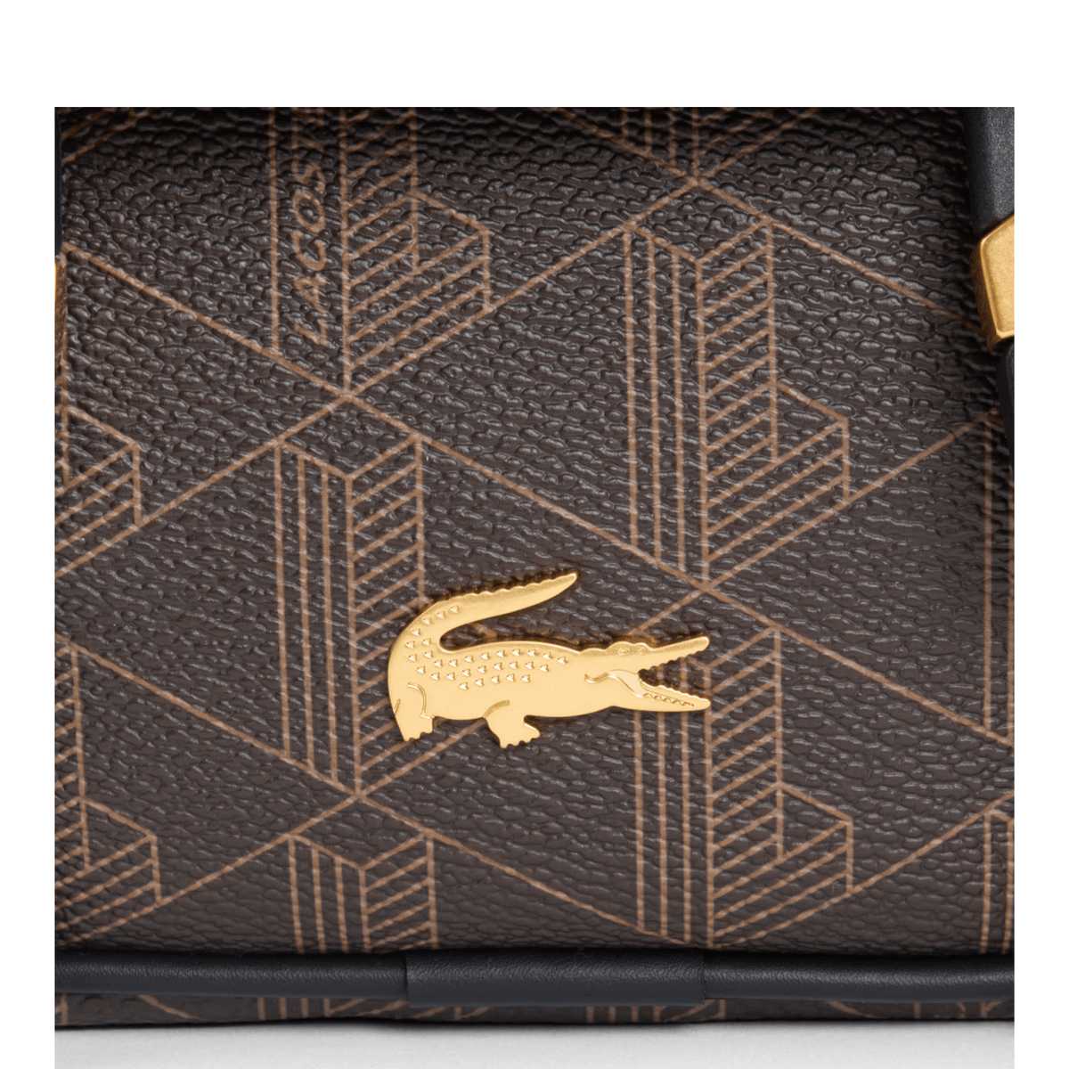 Gros plan sur le crocodile métallique doré et le monogramme grainé du sac Lacoste The Blend marron.