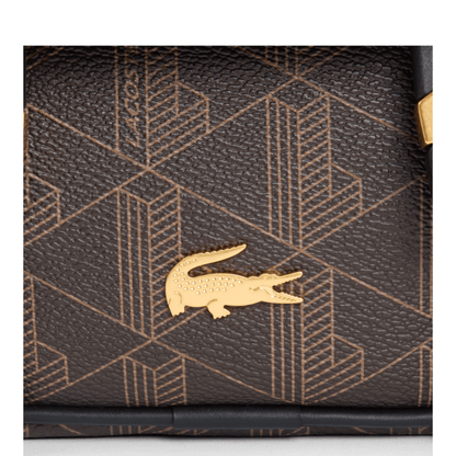 Gros plan sur le crocodile métallique doré et le monogramme grainé du sac Lacoste The Blend marron.