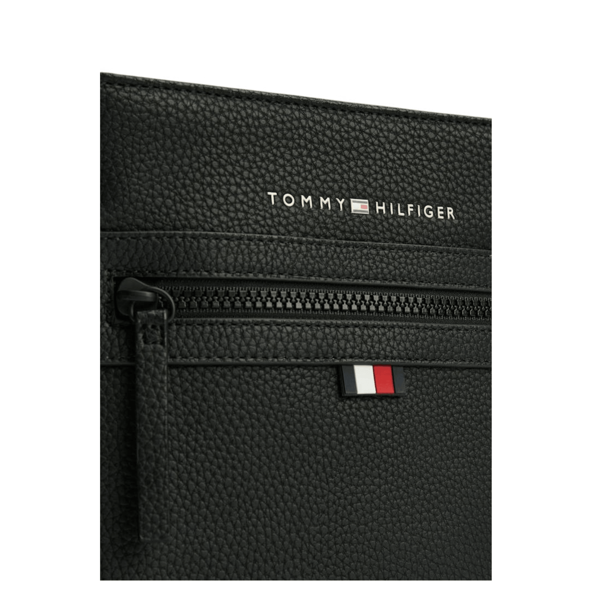 Gros plan sur le logo Tommy Hilfiger, le drapeau signature et la finition grainée de la sacoche noire AM0AM09505