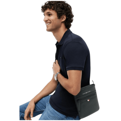 Homme portant la sacoche plate noire Tommy Hilfiger AM0AM09505 en bandoulière avec polo bleu marine