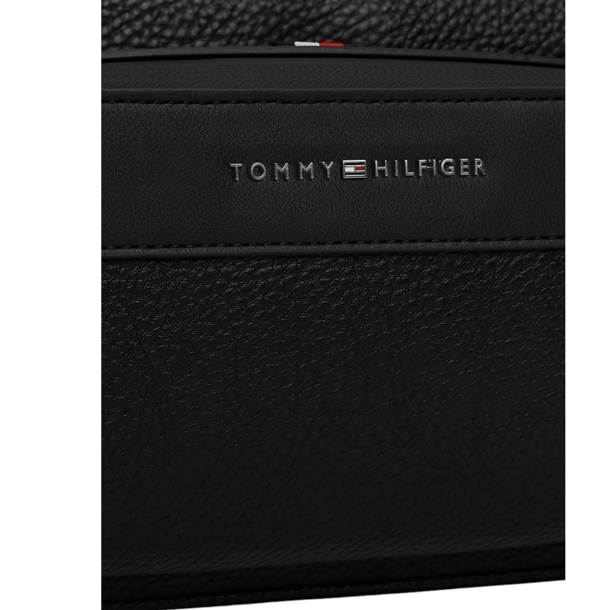 Gros plan sur le logo métallique Tommy Hilfiger et la matière effet cuir grainé de la sacoche noire