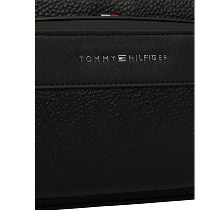 Gros plan sur le logo métallique Tommy Hilfiger et la matière effet cuir grainé de la sacoche noire